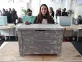 Una mujer muestra un baúl pintado a la tiza con un acabado desgastado. Otros baúles decorados se ven en el fondo.