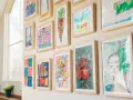 Un colorido cuadro para niños exhibe dibujos de helados, flores y retratos, cada uno enmarcado en madera clara.