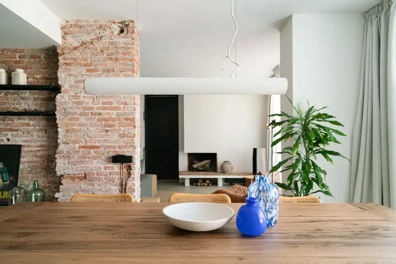 Salón con pared de ladrillo visto, mesa de madera con jarrones y planta.