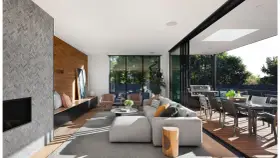 Elegante salón con chimenea de piedra, pared de madera y grandes ventanales que conectan con una terraza. Un ejemplo de las últimas tendencias interiorismo.