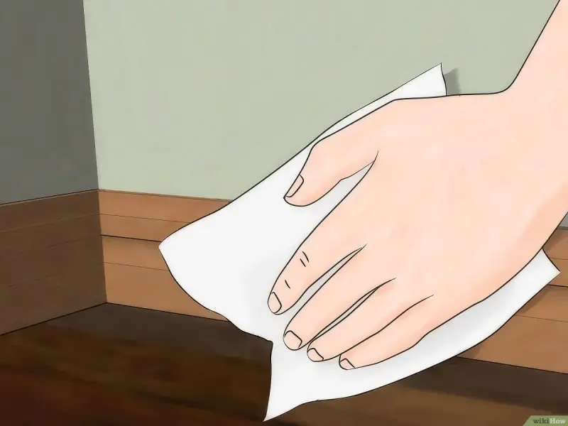 Mano limpiando rodapiés de pintura con un paño blanco.