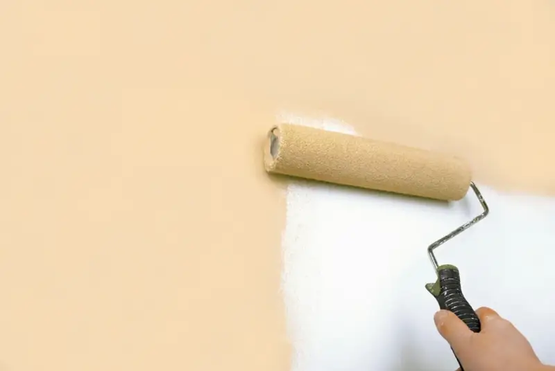 Rodillo pintando una pared de color melocotón con pintura blanca, buscando la mejor pintura antiruido para un hogar tranquilo.